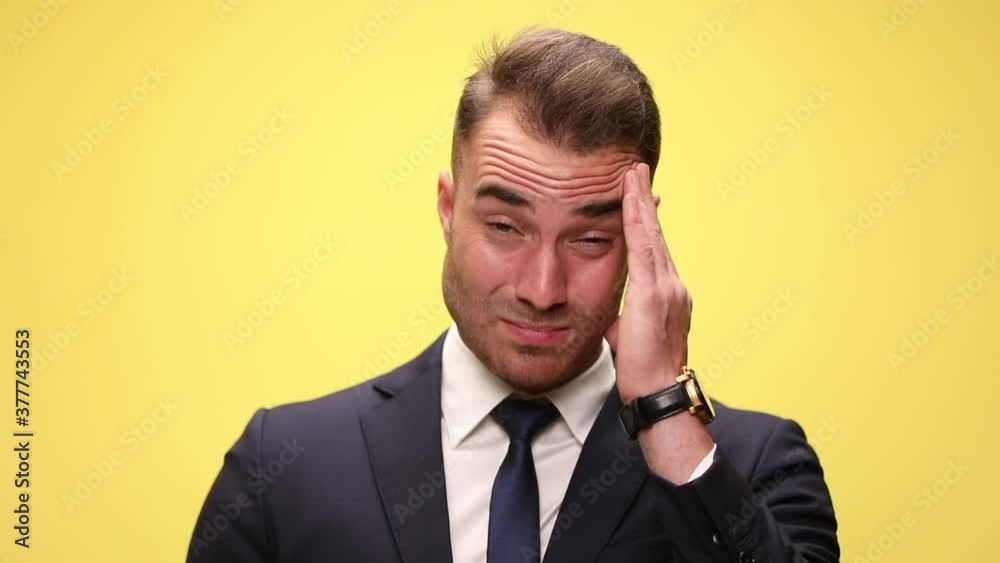 close up on a businessman rubbing his forehead and looking away on yellow background close up on a businessman rubbing his forehead and looking away on yellow background