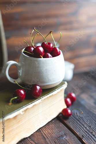 Fresh red ripe organic macro sweet cherry with waterd drops in a white cup on wooden background. space for text. closeup photo