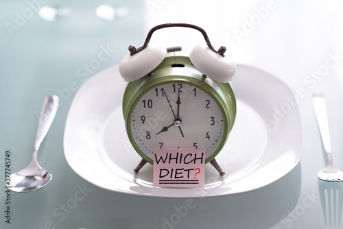 Question which diet to choose for your body concept with alarm clock and plate on a table