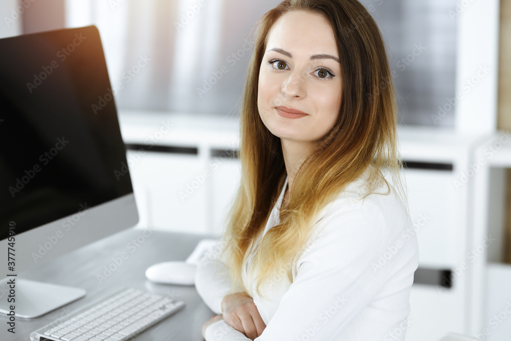Business woman headshot in sunny office. Unknown businesswoman sitting behind computer monitor