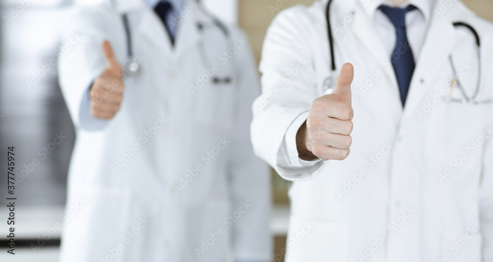 Group of modern doctors standing as a team with thumbs up or Ok sign in hospital office, close-up. Medical help, insurance in health care and medicine concept Group of modern doctors standing as a team with thumbs up or Ok sign in hospital office, close-up. Medical help, insurance in health care and medicine concept