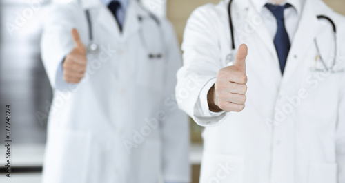 Group of modern doctors standing as a team with thumbs up or Ok sign in hospital office, close-up. Medical help, insurance in health care and medicine concept