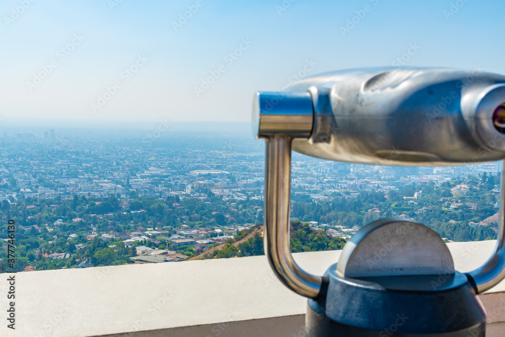 City landscape view downtown Los Angeles California with commercial and residential buildings and hazy skyline. Blurred unoccupied coin operated binoculars in foreground.