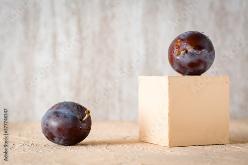 Creative still life. Ripe blue plum on a beige cube and one plum on the table. The importance of vitamins