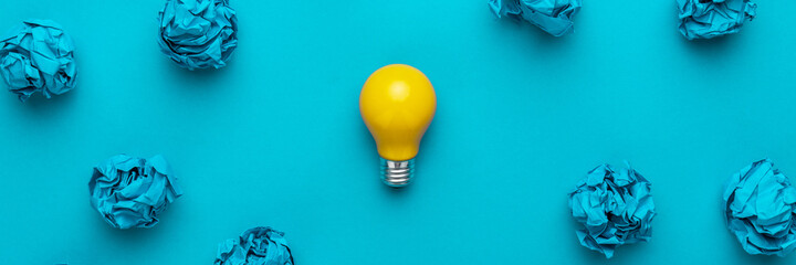 New idea concept with crumpled office paper and light bulb. Top view of great business idea concept over blue background. Creative solution during brainstorming session concept.
