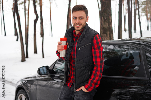 Attractive Caucasian man stands in winter forest near his car.