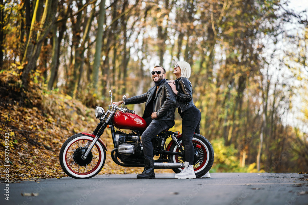 Pretty couple near red motorcycle on the road in the forest with colorful blured background