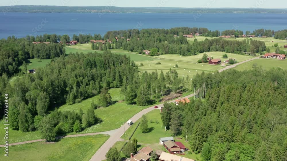 Swedish countryside with red wooden houses and summer fields. Blue clean lake and farms in aerial drone shot. Single car and motorhome caravan driving on small country road. Sweden dream on sunny day
