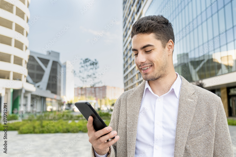 Young cheerful businessman in formalwear looking at screen of mobile phone Young cheerful businessman in formalwear looking at screen of mobile phone