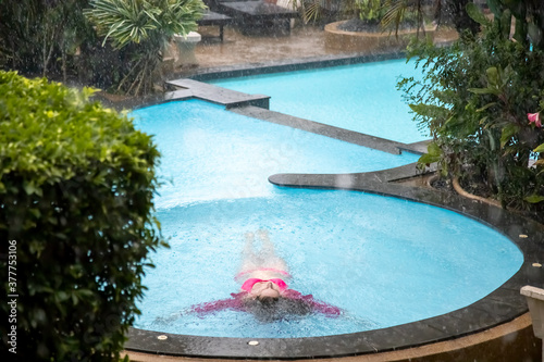 young girl lies in the water of a tropical outdoor pool in the pouring rain © Maria