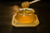 Honey drips from a honey stick into a glass pot. Thick honey dipped in a wooden honey spoon, close-up.