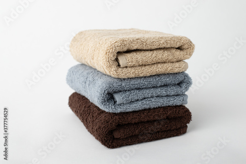 Stack of three bath cotton towels isolated on a white background. Beige, grey and brown terry towels to wipe and absorb water.