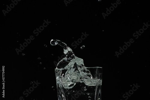 splash of water in a glass by ice cube on black background