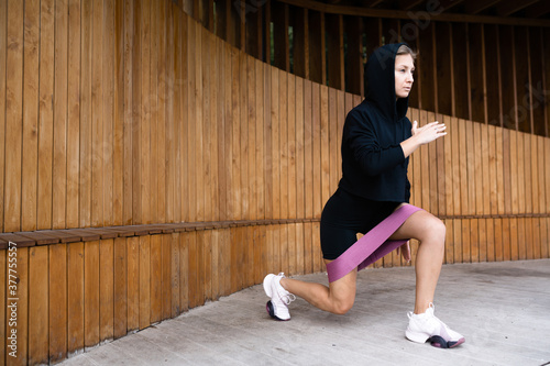 Girl in black sports uniform lunges with a fitness rubber band