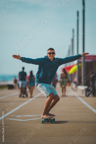 Happy carefree skater in a hoodie and sunglasses rides a longboard. Summer fun activities concept.