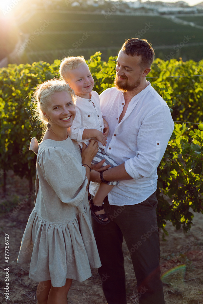family of three in light clothes stand in a grape field