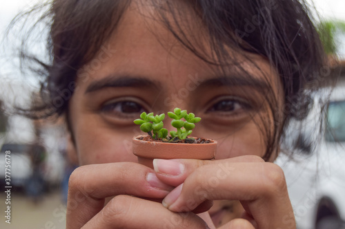 Young Hispanic woman holds a small plant in front of her. Concept love of plants.