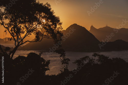 Beautiful view the sea and a chain of mountains silhouette at sunset against orange sky; Mount Corcovado, Rio de Janeiro, Brazil. Trees and vegetation silhouette in the foreground. Copy space for text