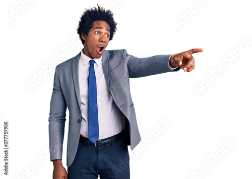 Handsome african american man with afro hair wearing business jacket pointing with finger surprised ahead, open mouth amazed expression, something on the front