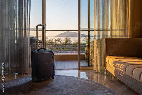 travel bag suitcase luggage in front of window in luxury hotel room with seaview on sunrise