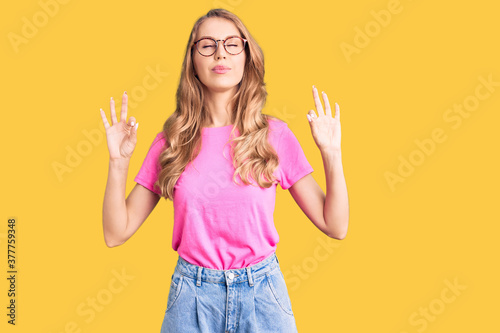 Young beautiful caucasian woman with blond hair wearing casual clothes and glasses relax and smiling with eyes closed doing meditation gesture with fingers. yoga concept.