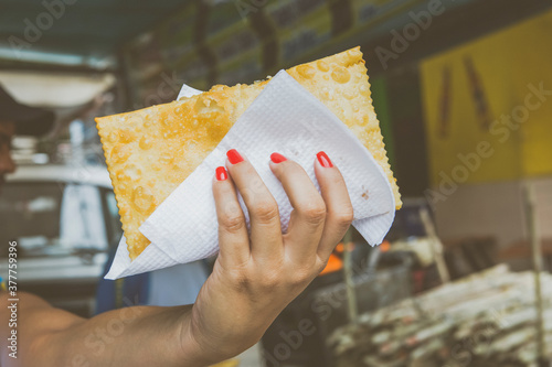 Female hand holding pastel at the free fair of Jardim Botânico, Rio de Janeiro, Brazil. Street food reinventing oneself new normal job during and after covid 19 pandemic concept. photo