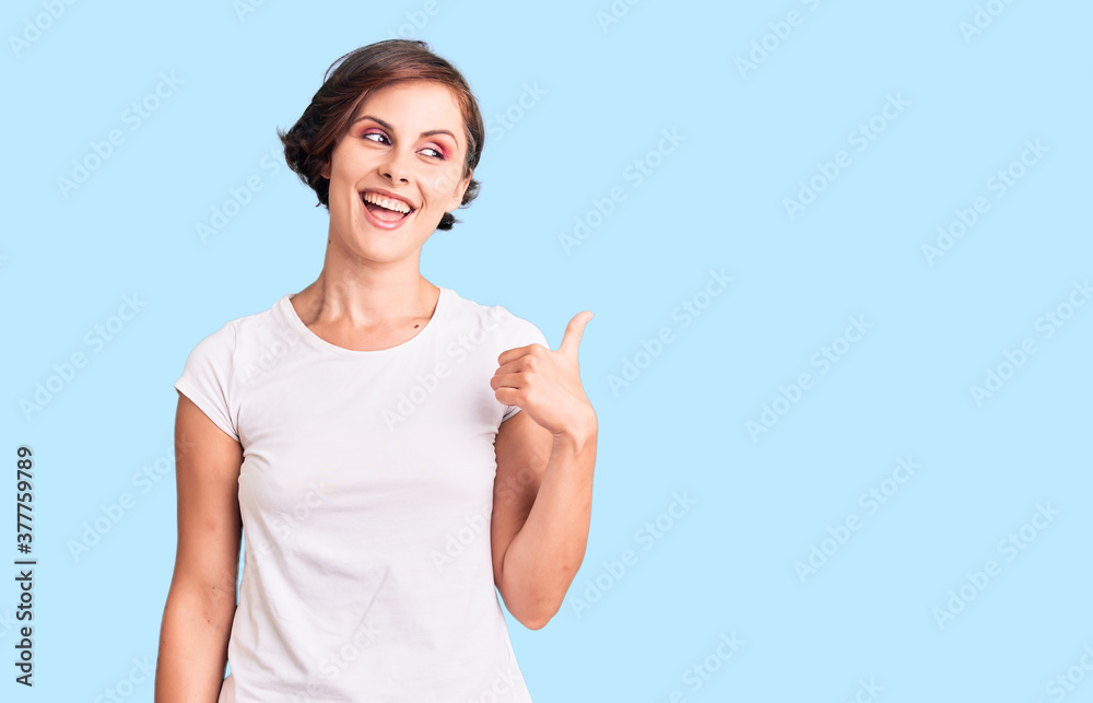 Beautiful young woman with short hair wearing casual clothes smiling with happy face looking and pointing to the side with thumb up. Beautiful young woman with short hair wearing casual clothes smiling with happy face looking and pointing to the side with thumb up.