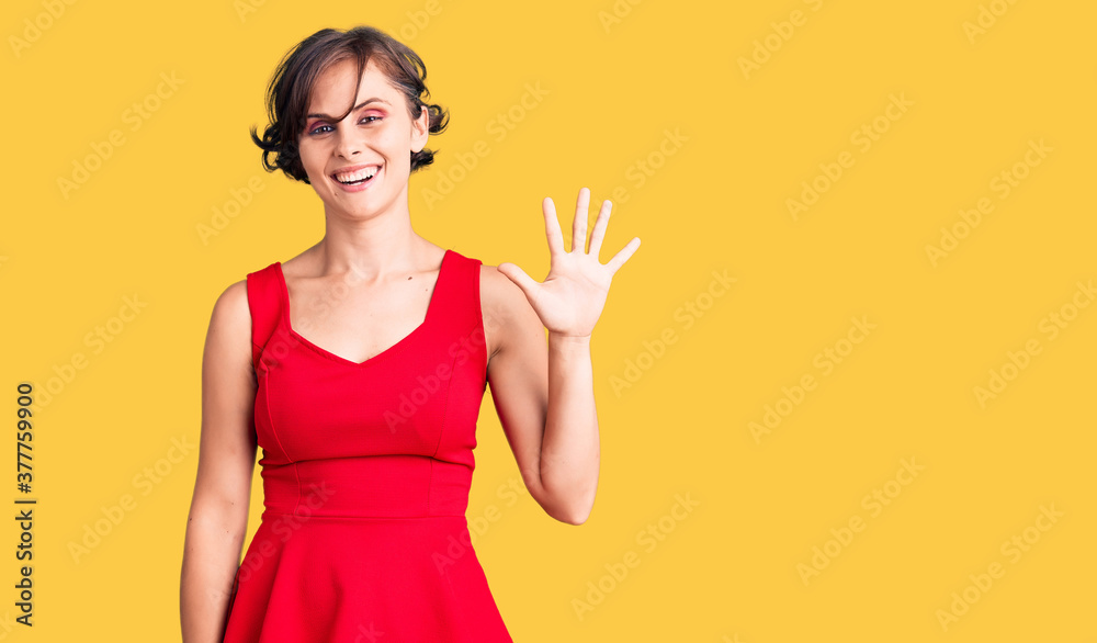 Beautiful young woman with short hair wearing casual style with sleeveless shirt showing and pointing up with fingers number five while smiling confident and happy. Beautiful young woman with short hair wearing casual style with sleeveless shirt showing and pointing up with fingers number five while smiling confident and happy.