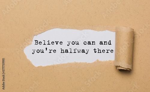 The text Believe you can and you're halfway there, appearing behind torn paper. Motivational quote. The craft paper is ripped. photo