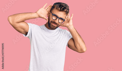Young hispanic man wearing casual clothes and glasses trying to hear both hands on ear gesture, curious for gossip. hearing problem, deaf photo