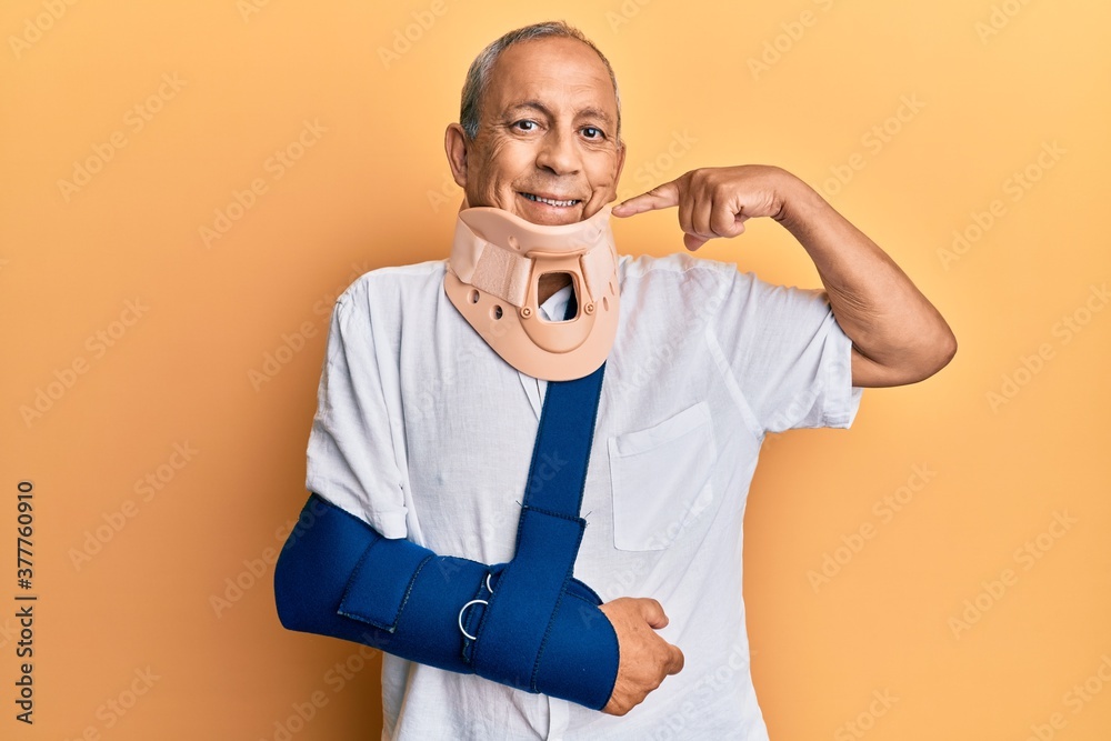 Handsome mature senior man wearing cervical collar and arm on sling smiling cheerful showing and pointing with fingers teeth and mouth. dental health concept. Handsome mature senior man wearing cervical collar and arm on sling smiling cheerful showing and pointing with fingers teeth and mouth. dental health concept.