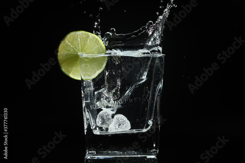 splash of water with lime in a glass over ice cube on black background