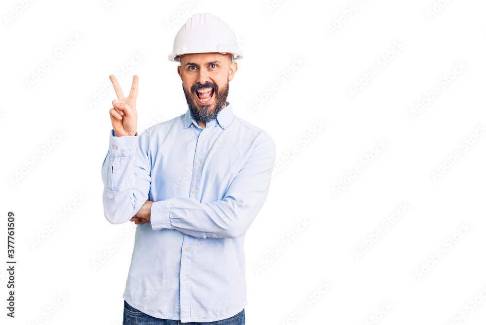 Young handsome man wearing architect hardhat smiling with happy face winking at the camera doing victory sign. number two. Young handsome man wearing architect hardhat smiling with happy face winking at the camera doing victory sign. number two.