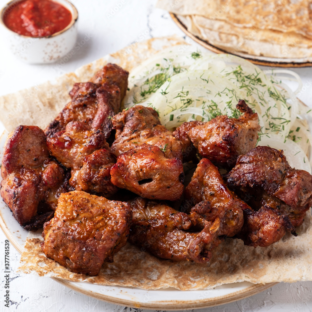 Meat shish kebab on a plate. Sashlik  with red sauce. Closeup