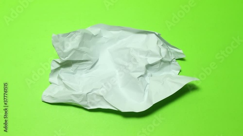 crumpled paper ball on green background.  The screen wrinkles as a ball of paper and leaves the screen jumping. And, a sheet of paper enters the screen as a ball and unwrap itself filling the screen. 