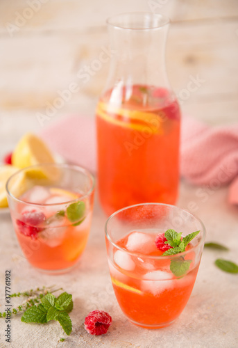 Due bicchieri e caraffa con aperitivo con scorza di limone  lamponi  menta e ghiaccio 