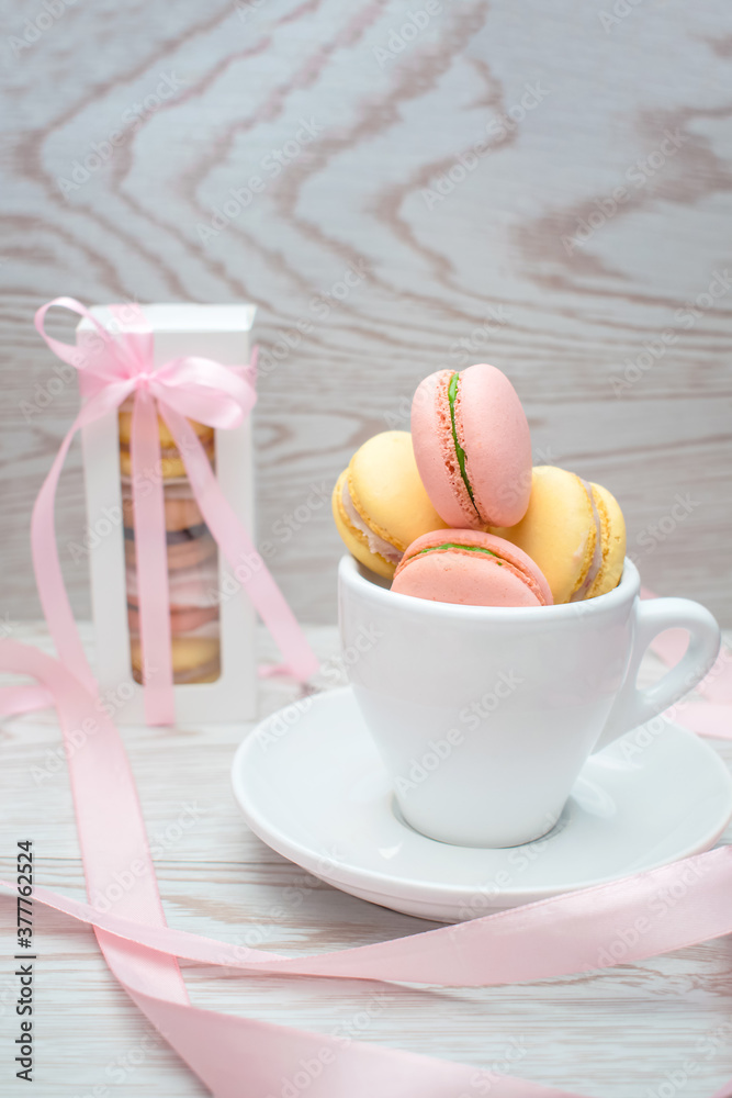 sweet macaroons in cup and in gift box in wooden background, dessert concept