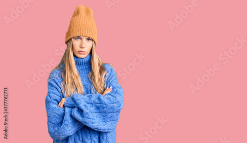 Beautiful caucasian woman with blonde hair wearing wool sweater and winter hat skeptic and nervous, disapproving expression on face with crossed arms. negative person.