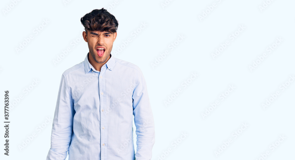 Young hispanic man wearing casual shirt winking looking at the camera with sexy expression, cheerful and happy face. Young hispanic man wearing casual shirt winking looking at the camera with sexy expression, cheerful and happy face.