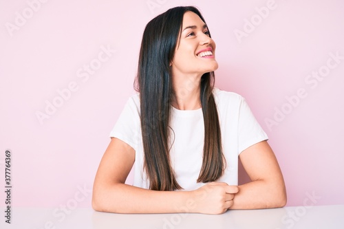 Young caucasian woman sitting at the table wearing casual white tshirt looking to side, relax profile pose with natural face with confident smile.