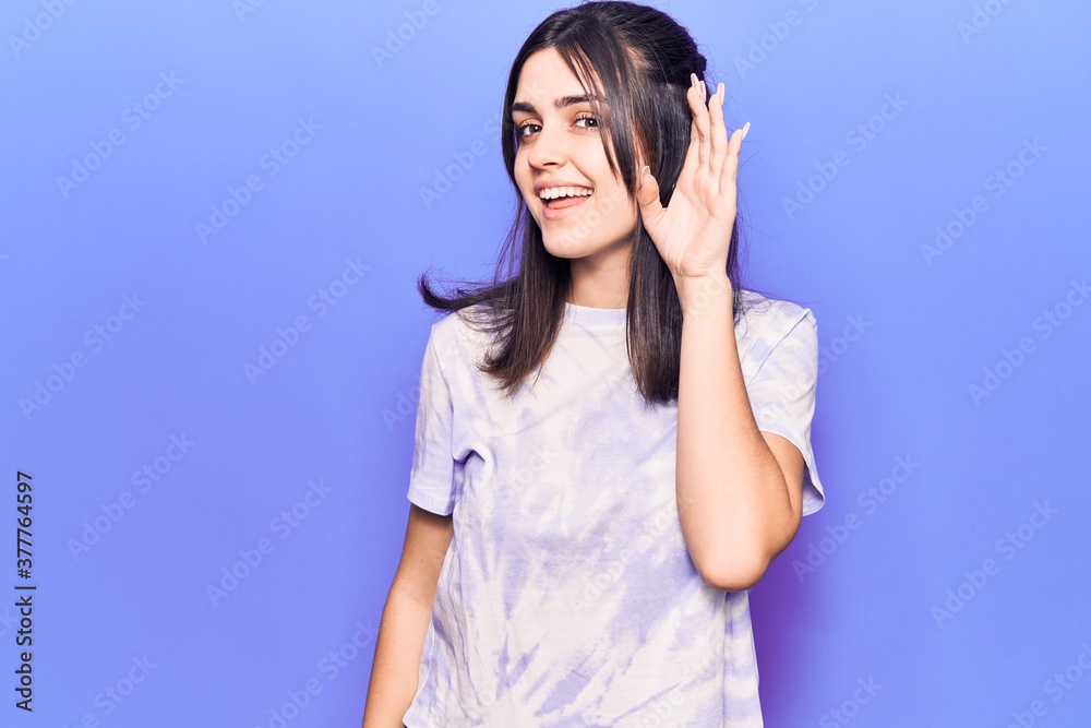 Young beautiful girl wearing casual t shirt smiling with hand over ear listening and hearing to rumor or gossip. deafness concept.