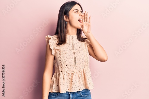 Young beautiful girl wearing casual sleeveles t shirt shouting and screaming loud to side with hand on mouth. communication concept. photo