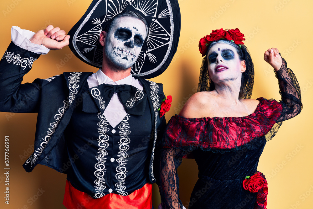 Young couple wearing mexican day of the dead costume over yellow stretching back, tired and relaxed, sleepy and yawning for early morning Young couple wearing mexican day of the dead costume over yellow stretching back, tired and relaxed, sleepy and yawning for early morning