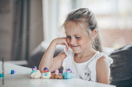 Little cute preschooler child girl playing educational games with plasticine figures preparing for school in kindergarten while sitting at table. Back to school concept.