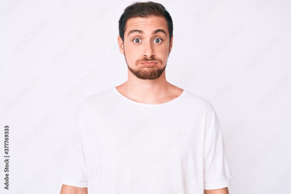 Young handsome man wearing casual white tshirt puffing cheeks with funny face. mouth inflated with air, crazy expression. Young handsome man wearing casual white tshirt puffing cheeks with funny face. mouth inflated with air, crazy expression.