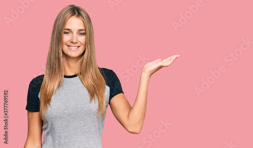 Young blonde woman wearing casual clothes smiling cheerful presenting and pointing with palm of hand looking at the camera.