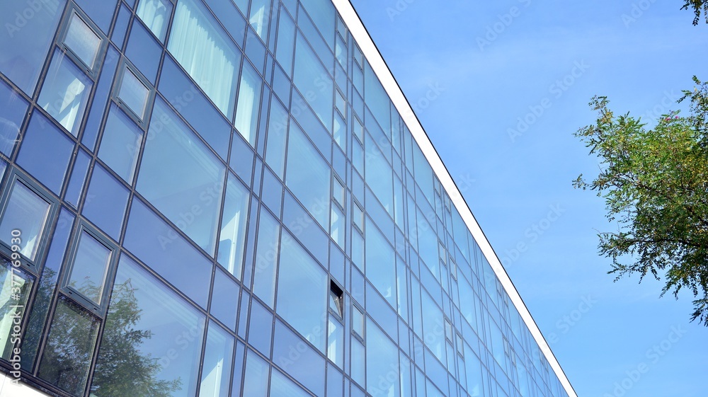 Blue curtain wall made of toned glass and steel constructions under blue sky. A fragment of a building. Blue curtain wall made of toned glass and steel constructions under blue sky. A fragment of a building.
