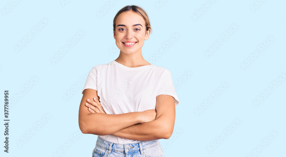 Young beautiful blonde woman wearing casual white tshirt happy face smiling with crossed arms looking at the camera. positive person. Young beautiful blonde woman wearing casual white tshirt happy face smiling with crossed arms looking at the camera. positive person.