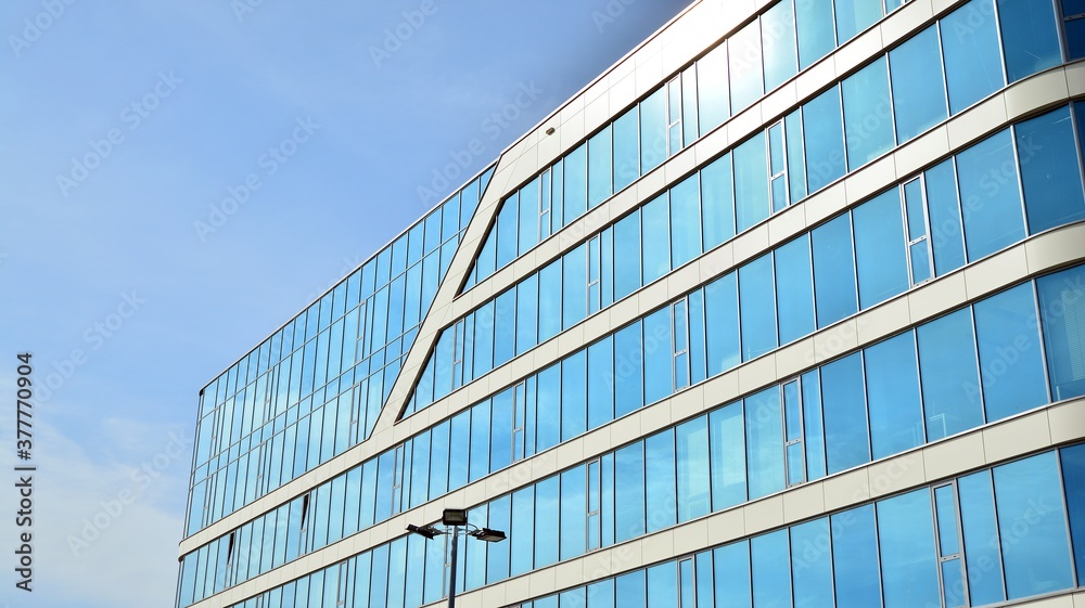 Blue curtain wall made of toned glass and steel constructions under blue sky. A fragment of a building. Blue curtain wall made of toned glass and steel constructions under blue sky. A fragment of a building.