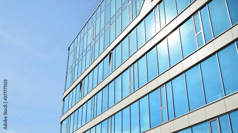 Blue curtain wall made of toned glass and steel constructions under blue sky. A fragment of a building.